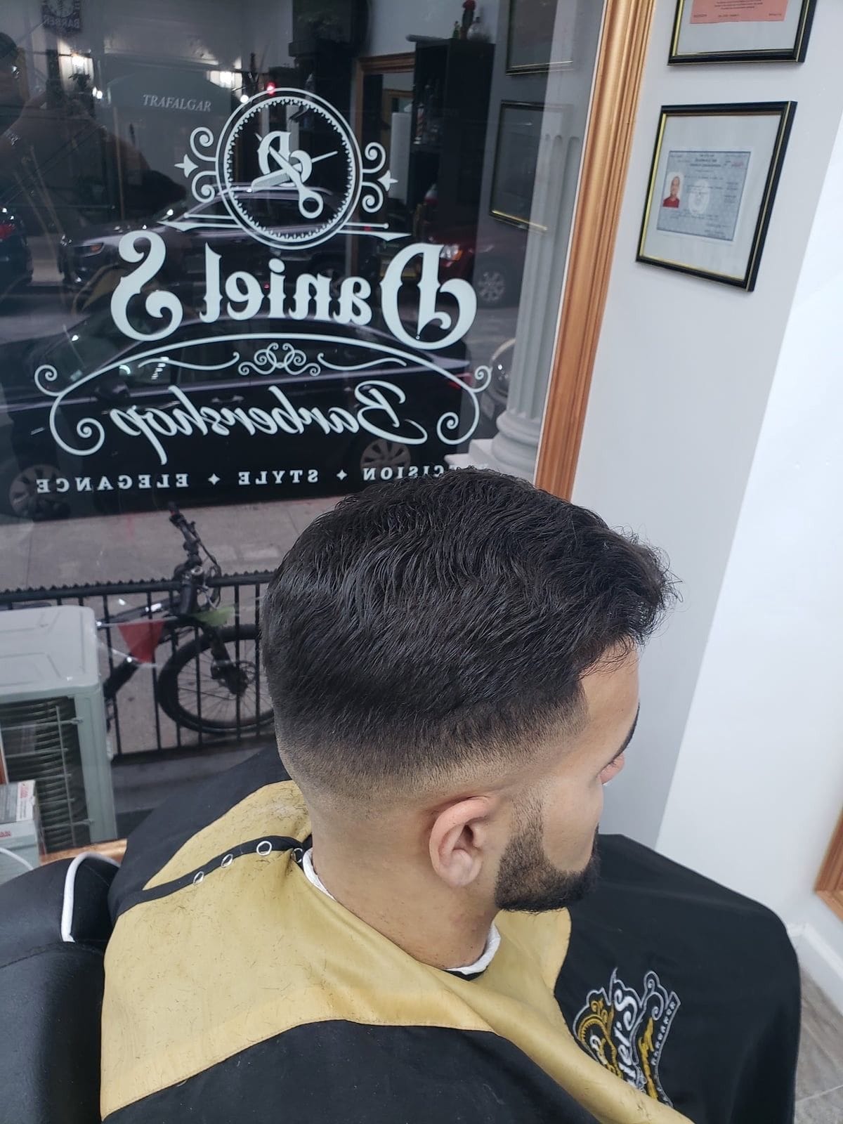 Side view of a clean fade and trimmed beard in front of the shop window with the Daniel’s logo