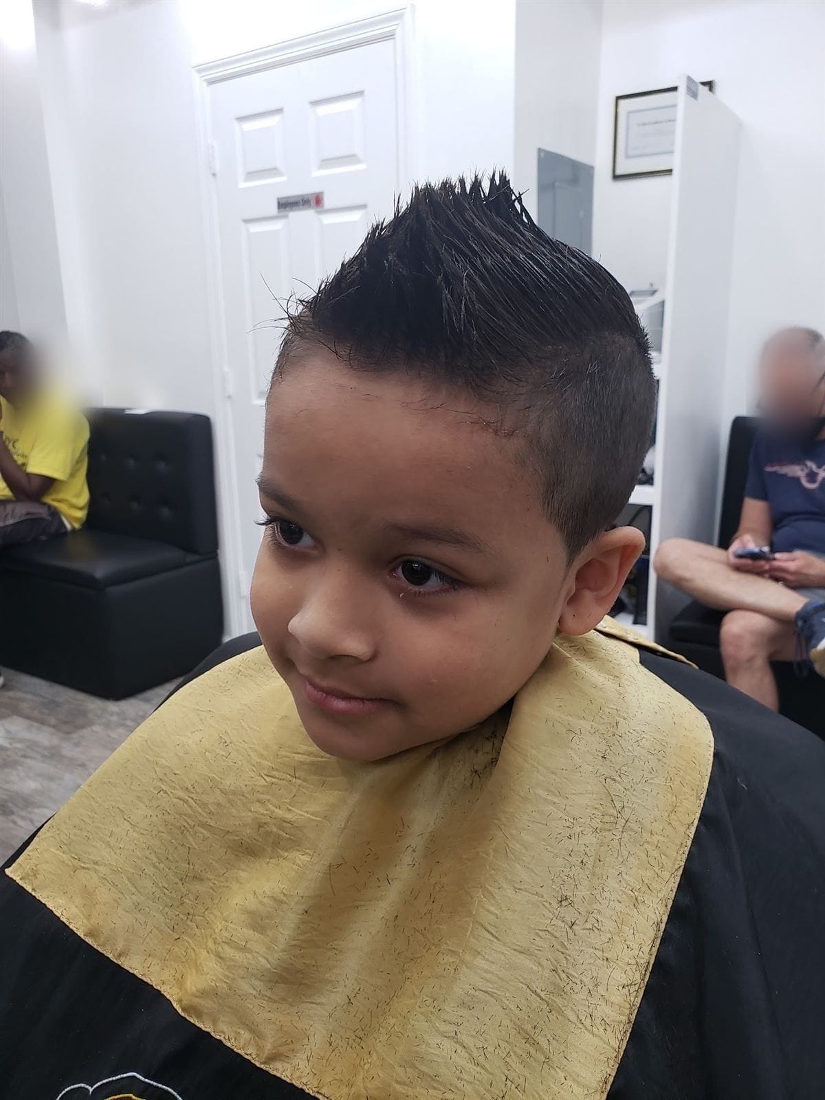 A young boy in the chair with a fresh spiked haircut, looking off to the side
