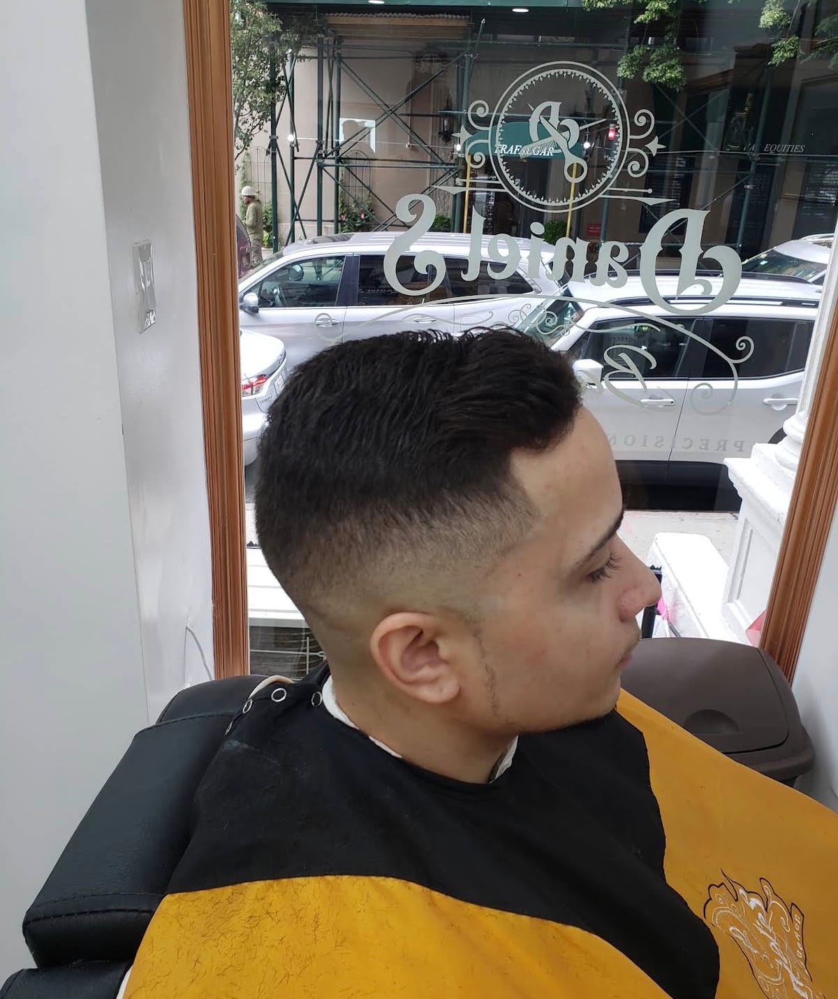 A clean skin fade seen from the side, with the Daniel’s logo on the window behind